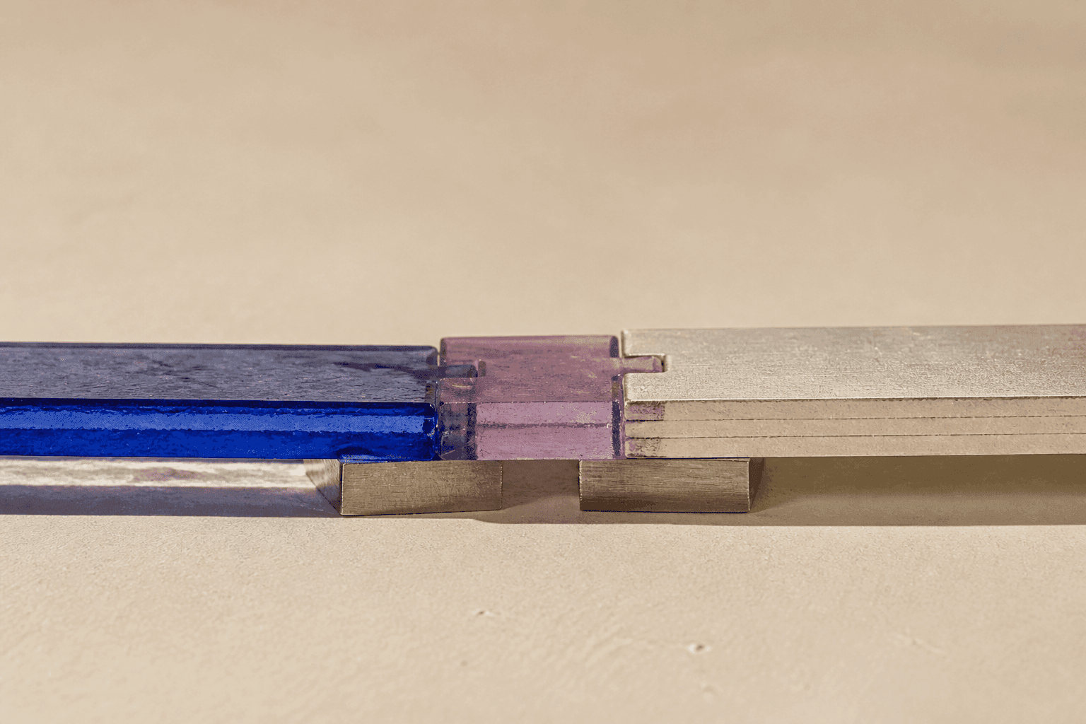 Nature morte générée en gros plan montrant une bande de verre cobalt et une pile de papier ivoire réunies par un joint de résine violette posé sur de petites cales d’aluminium.